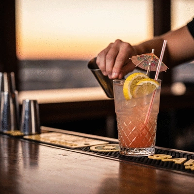 Refreshing cocktail with a Fort Myers sunset theme, garnished with citrus and a small umbrella, on a bar counter with blurred background of a lively happy hour scene, no text, no words, no typography, 8K